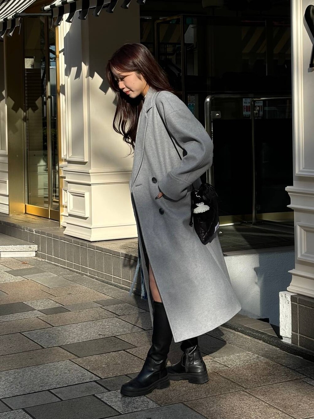 グレー系のチェスターコート、ブラック系のショルダーバッグ、ブルー系のマフラーを着用したレディースの冬コーディネートの6枚目の写真