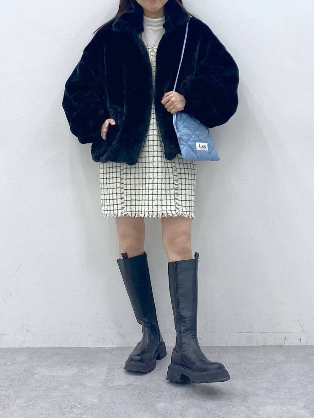 ブルー系のショルダーバッグ、ブラック系のブーツ、ベージュ系のTシャツ/カットソーを着用したレディースの冬コーディネートの2枚目の写真