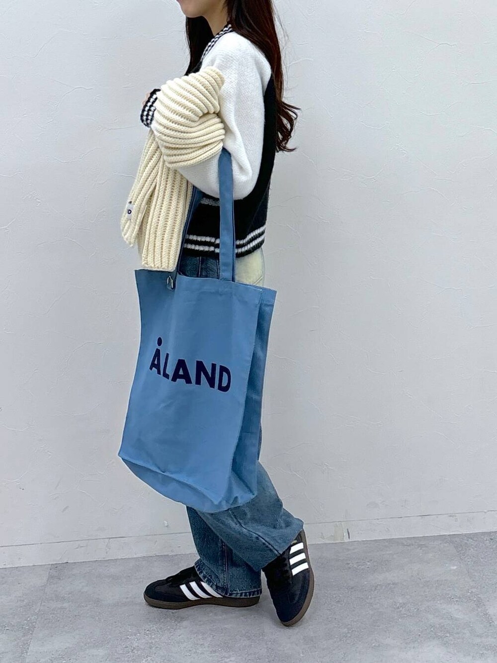 ブルー系のトートバッグ、ブルー系のデニムパンツ、ホワイト系のニット/セーターを着用したレディースの秋コーディネートの4枚目の写真