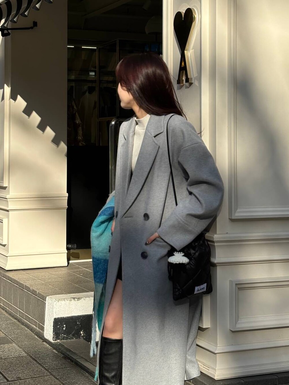 グレー系のチェスターコート、ブラック系のショルダーバッグ、ブルー系のマフラーを着用したレディースの冬コーディネートの7枚目の写真