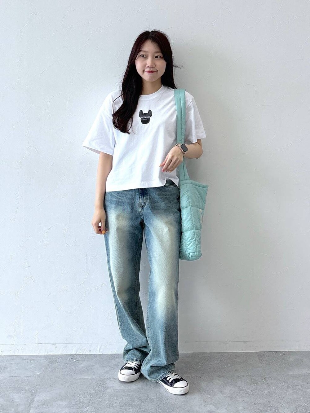 ブルー系のデニムパンツ、グリーン系のショルダーバッグ、ホワイト系のTシャツ/カットソーを着用したレディースの夏コーディネートの3枚目の写真