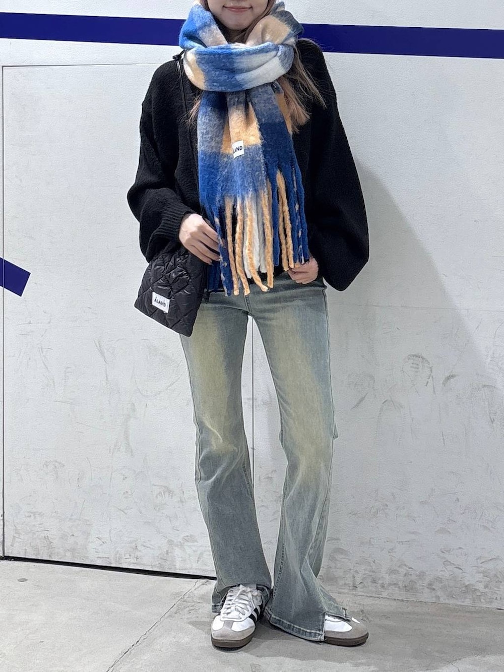 ブルー系のデニムパンツ、ブラック系のニット/セーター、ブラック系のショルダーバッグを着用したレディースの秋コーディネートの2枚目の写真