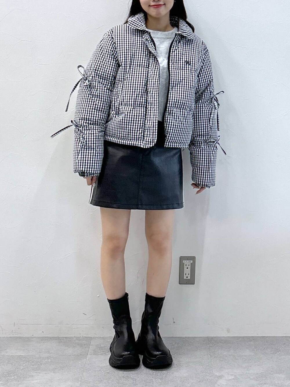 グレー系のニット/セーター、ブラック系のスカート、ブラック系のダウンジャケット/コートを着用したレディースの秋コーディネートの2枚目の写真