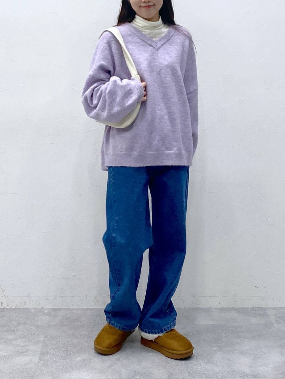 ブルー系のデニムパンツ、ベージュ系のTシャツ/カットソー、パープル系のニット/セーターを着用したレディースの冬コーディネートの2枚目の写真