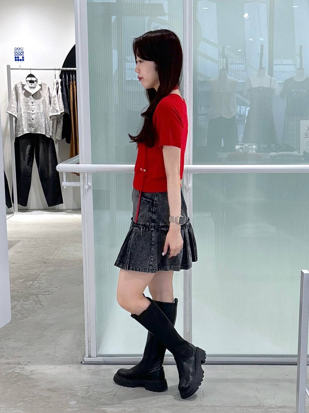レッド系のニット/セーター、ブラック系のブーツ、ブラック系のデニムスカートを着用したレディースの夏コーディネートの3枚目の写真