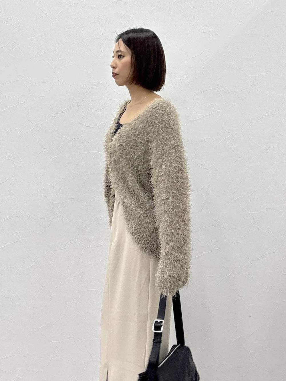 ブラック系のショルダーバッグ、ベージュ系のスカート、ゴールド系のピアス(両耳用)を着用したレディースの冬コーディネートの5枚目の写真