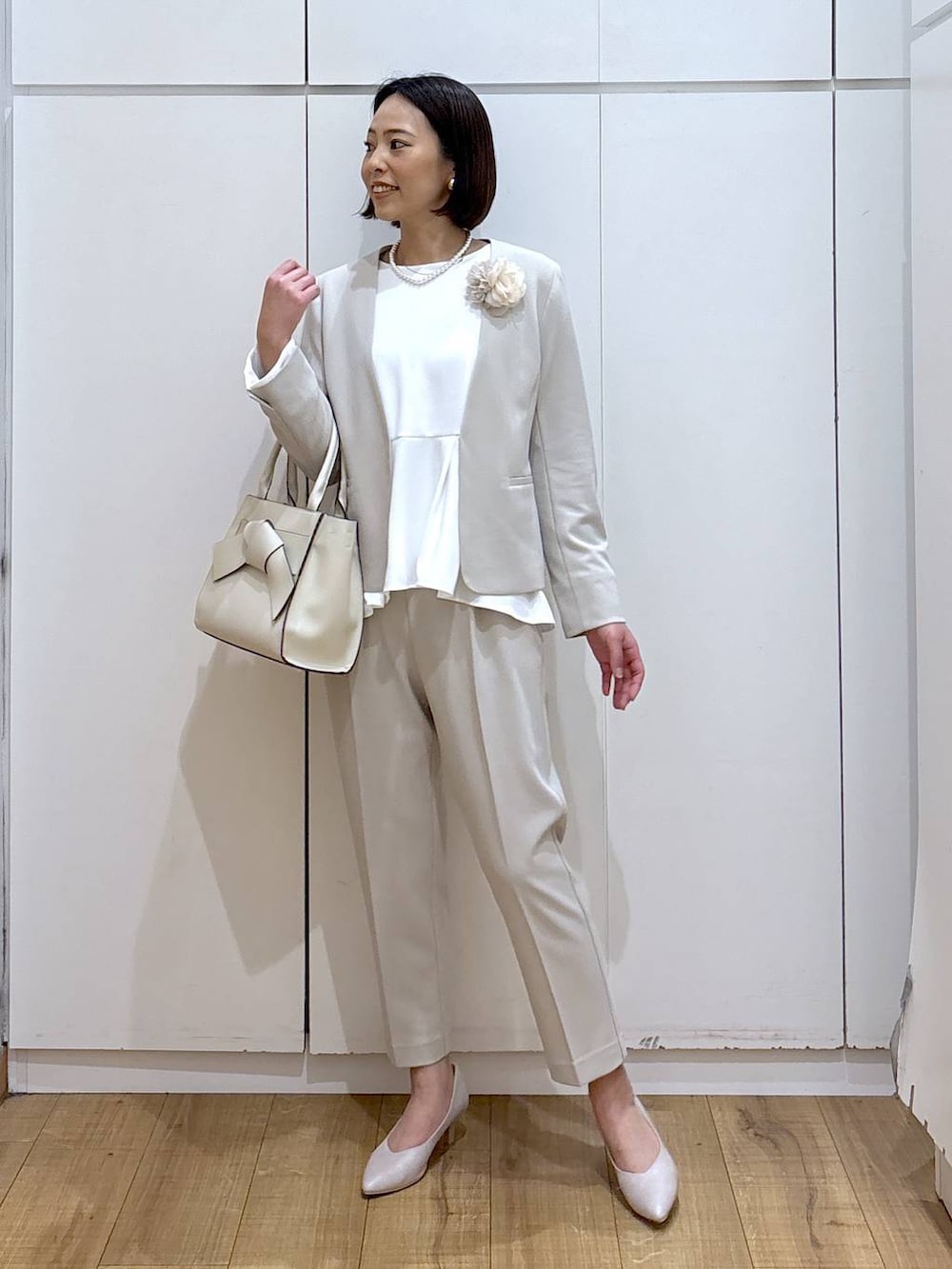 ホワイト系のパンプス、ベージュ系のセットアップ、ベージュ系のハンドバッグを着用したレディースの冬コーディネートの3枚目の写真
