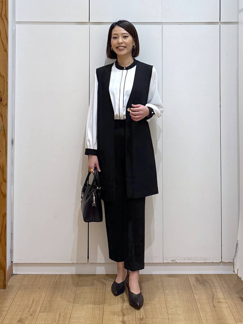 ブラック系のショルダーバッグ、ブラック系のパンプス、ブラック系のスラックスを着用したレディースの冬コーディネートの2枚目の写真