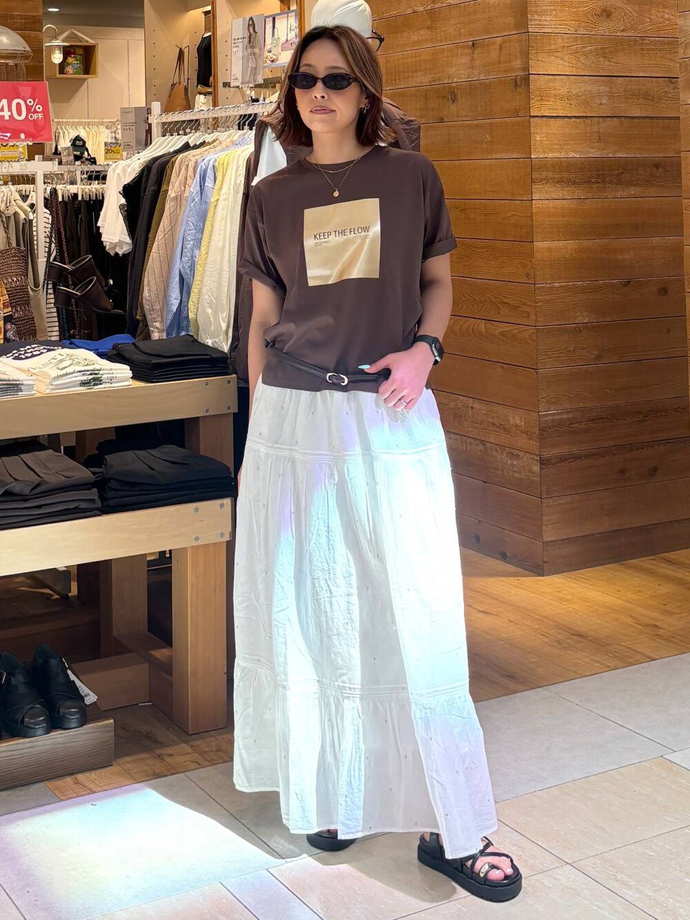 ホワイト系のスカート、ブラウン系のTシャツ/カットソー、ブラック系のサンダルを着用したレディースの春コーディネートの3枚目の写真