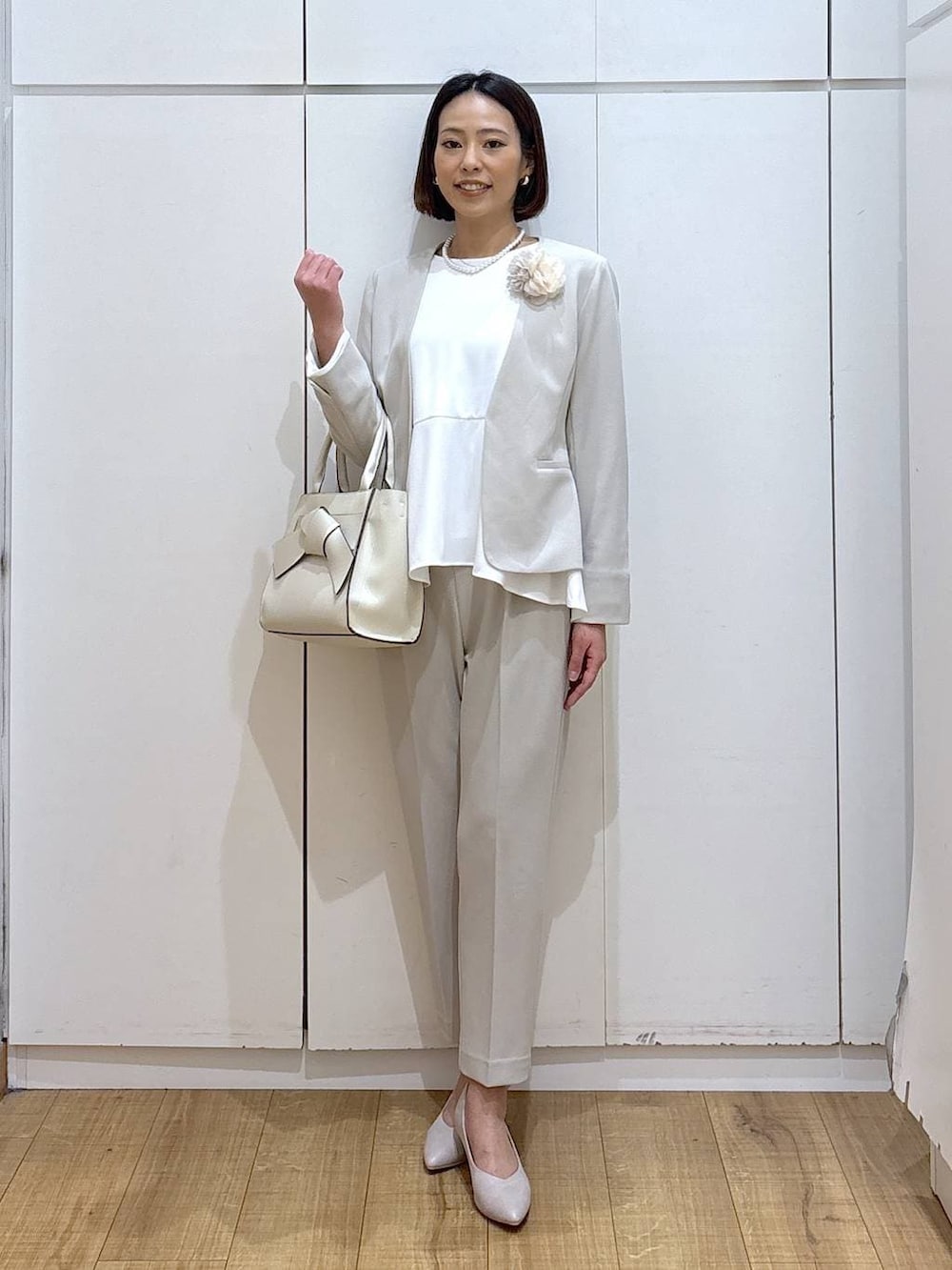 ホワイト系のパンプス、ベージュ系のセットアップ、ベージュ系のハンドバッグを着用したレディースの冬コーディネートの2枚目の写真
