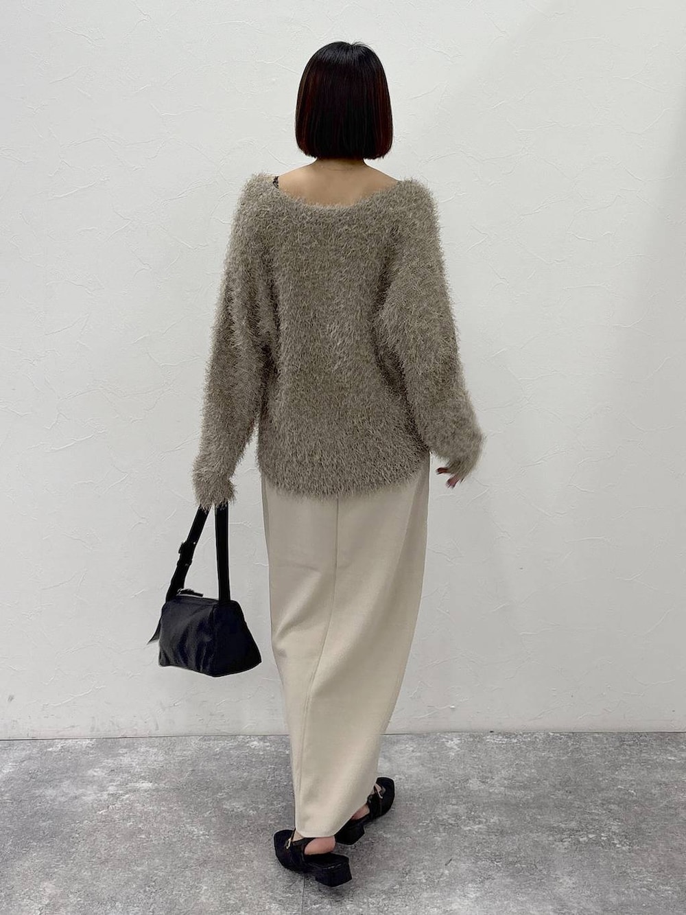 ブラック系のショルダーバッグ、ベージュ系のスカート、ゴールド系のピアス(両耳用)を着用したレディースの冬コーディネートの9枚目の写真