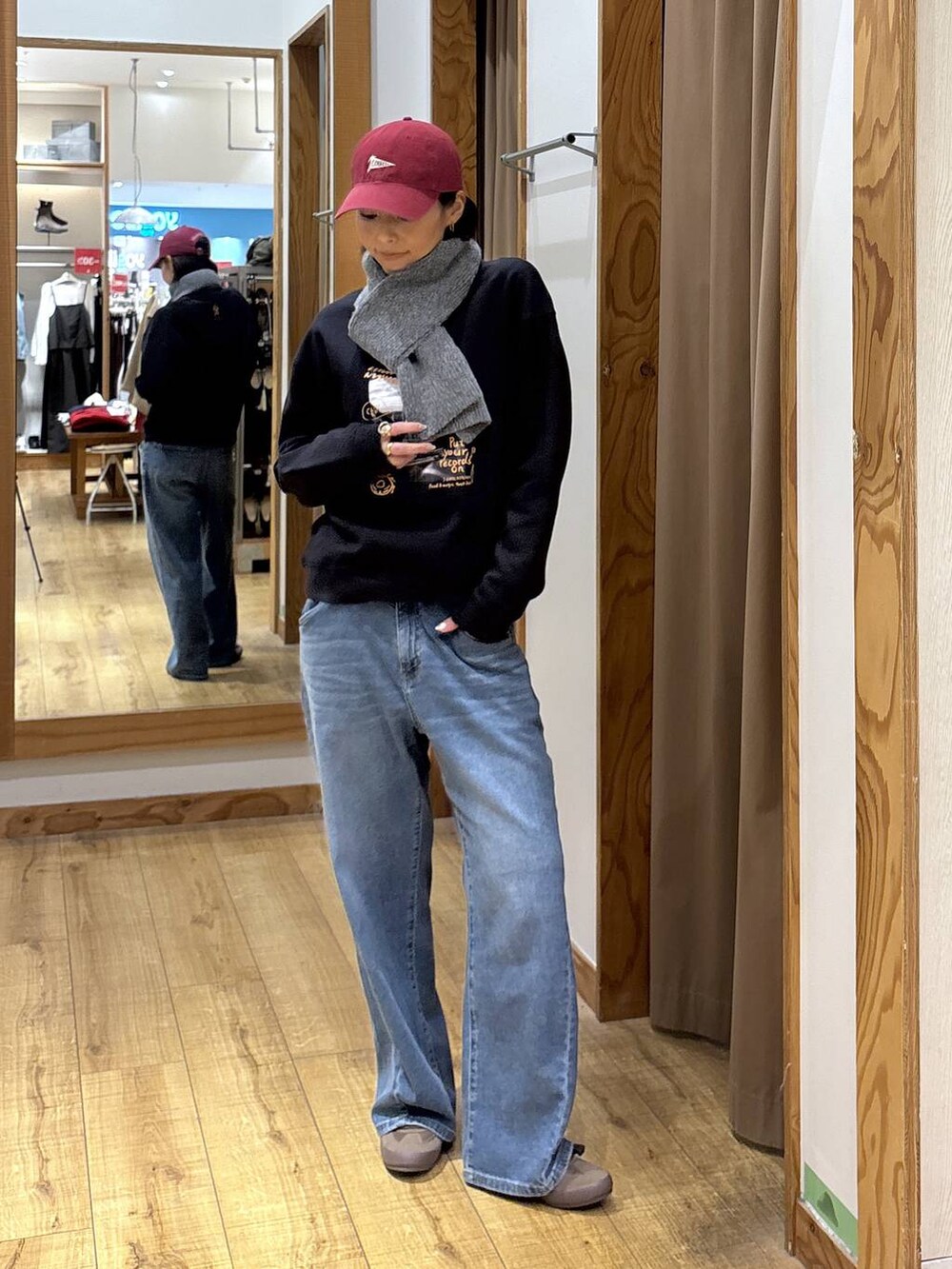 グレー系のスウェット、ブルー系のデニムパンツ、レッド系のハットを着用したレディースの秋コーディネートの2枚目の写真
