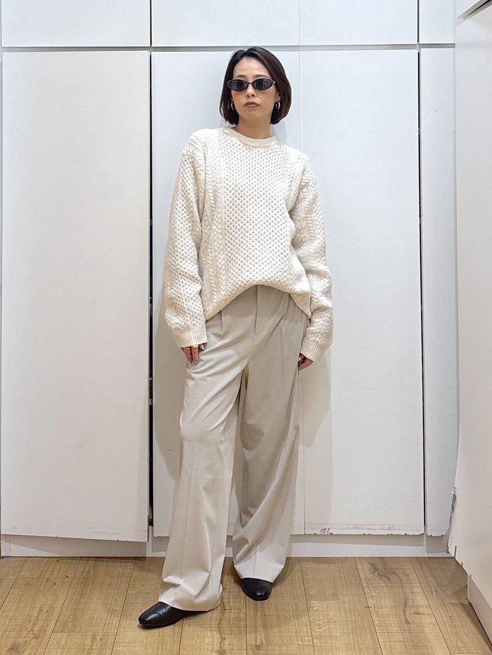 ベージュ系のスラックス、ブラック系のブーツ、ホワイト系のニット/セーターを着用したレディースの冬コーディネートの2枚目の写真