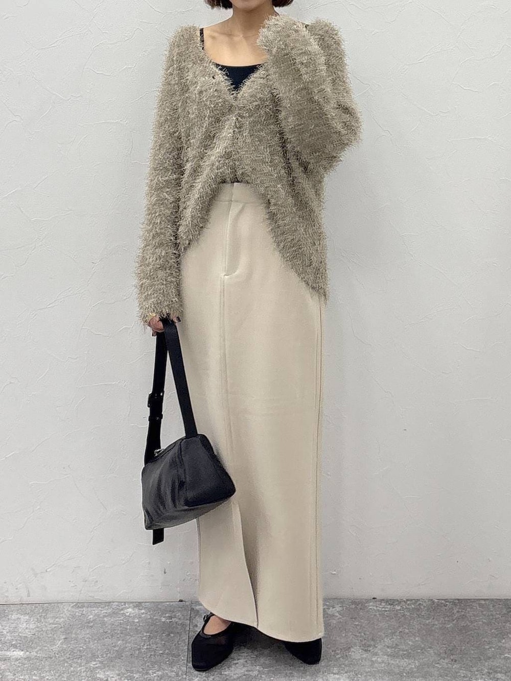 ブラック系のショルダーバッグ、ベージュ系のスカート、ゴールド系のピアス(両耳用)を着用したレディースの冬コーディネートの2枚目の写真