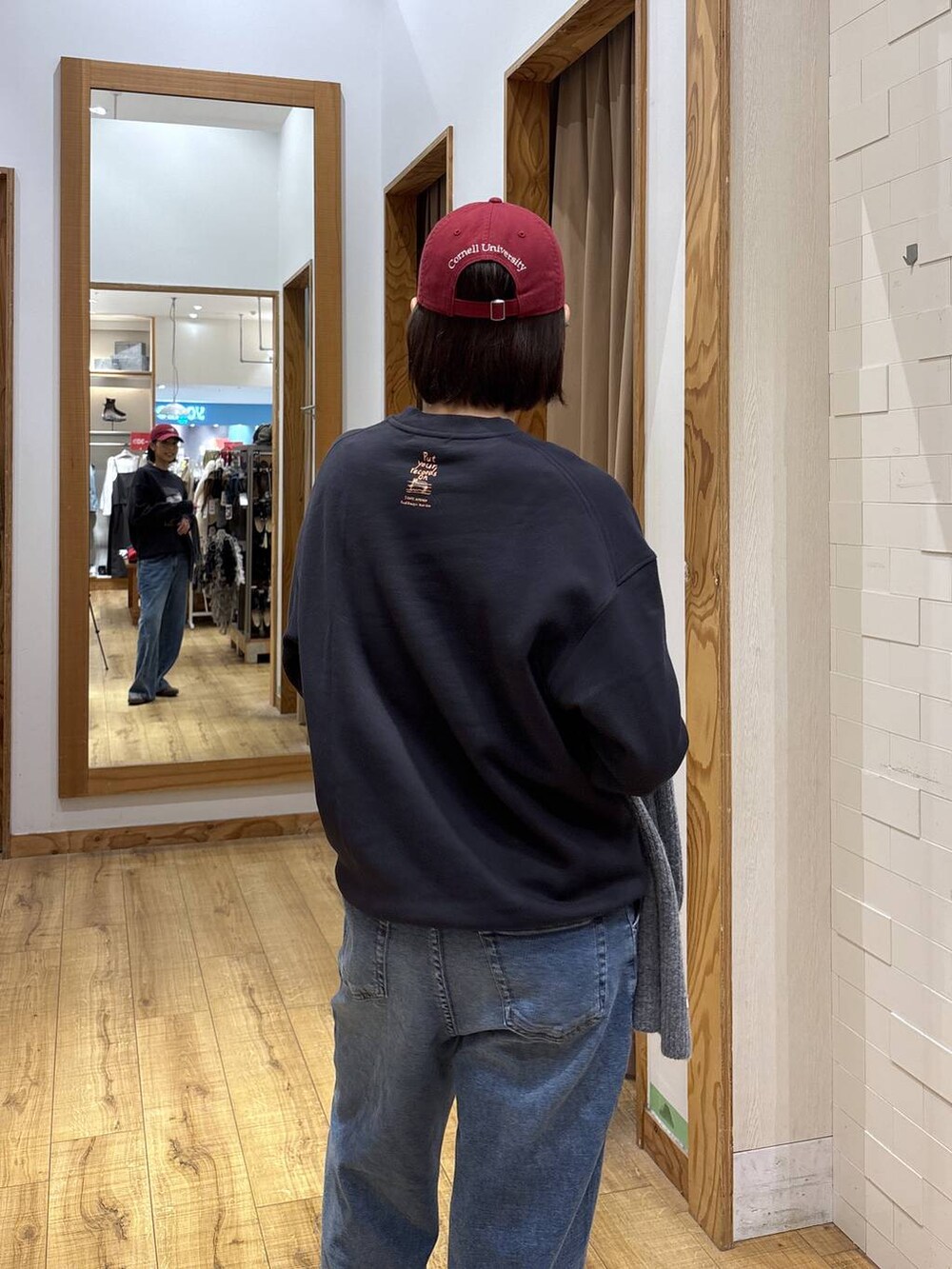 グレー系のスウェット、ブルー系のデニムパンツ、レッド系のハットを着用したレディースの秋コーディネートの7枚目の写真