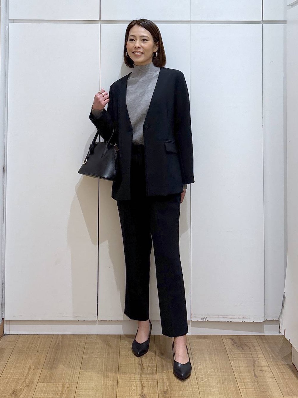 ブラック系のショルダーバッグ、ブラック系のパンプス、グレー系のニット/セーターを着用したレディースの冬コーディネートの2枚目の写真