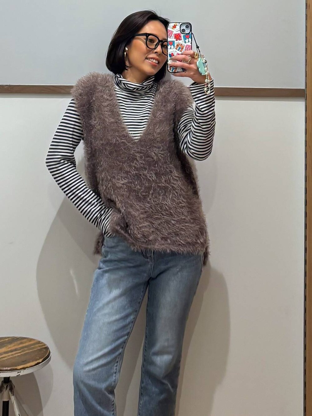 ブルー系のデニムパンツ、ブラウン系のベスト、ゴールド系のピアス（両耳用）を着用したレディースの秋コーディネートの3枚目の写真