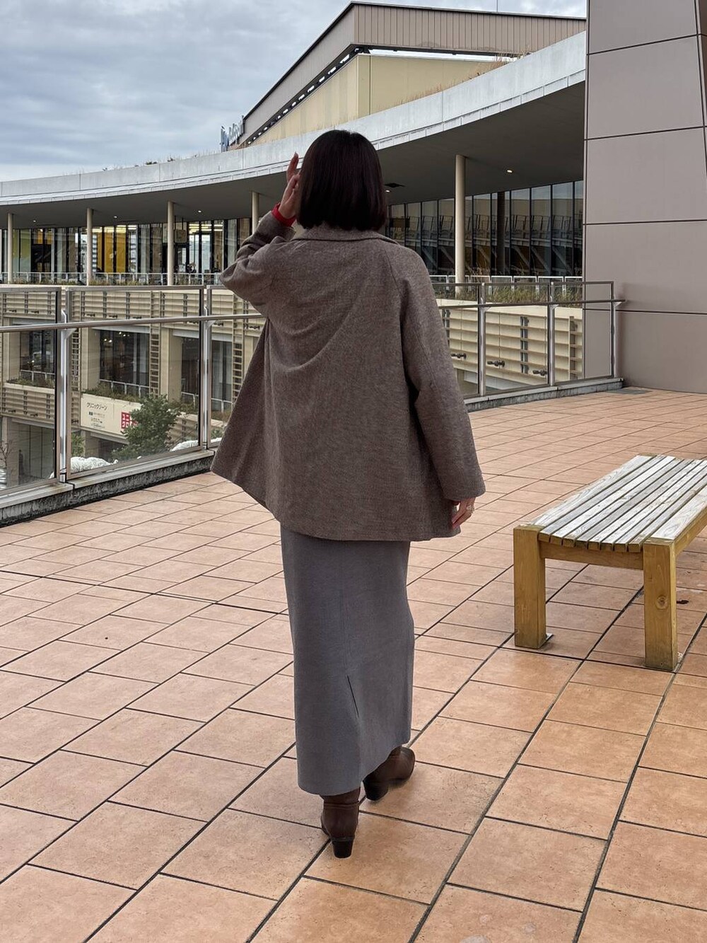 ブラウン系のチェスターコート、グレー系のスカート、ホワイト系のTシャツ/カットソーを着用したレディースの秋コーディネートの4枚目の写真