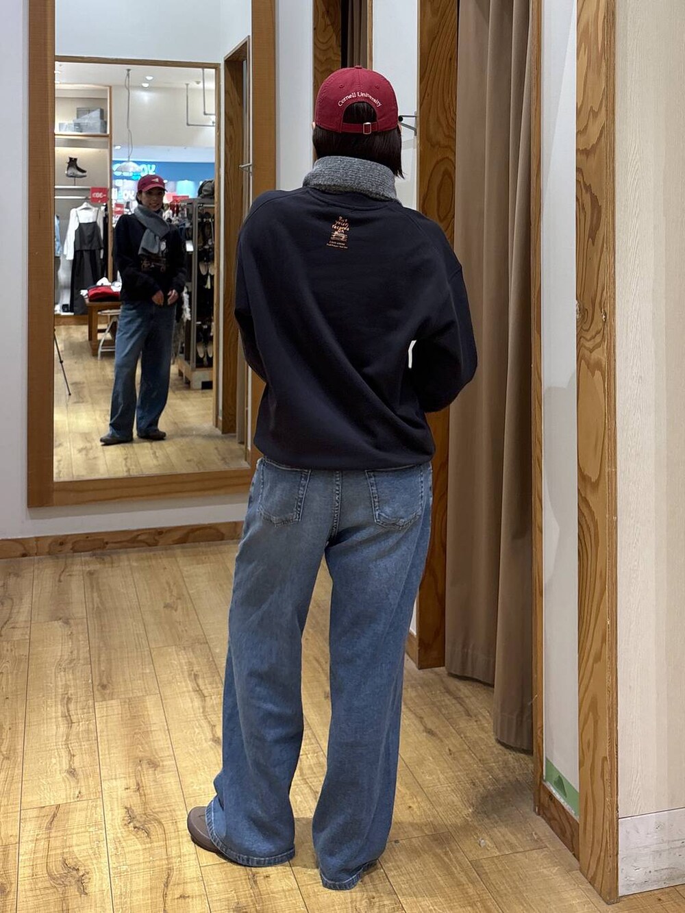 グレー系のスウェット、ブルー系のデニムパンツ、レッド系のハットを着用したレディースの秋コーディネートの4枚目の写真