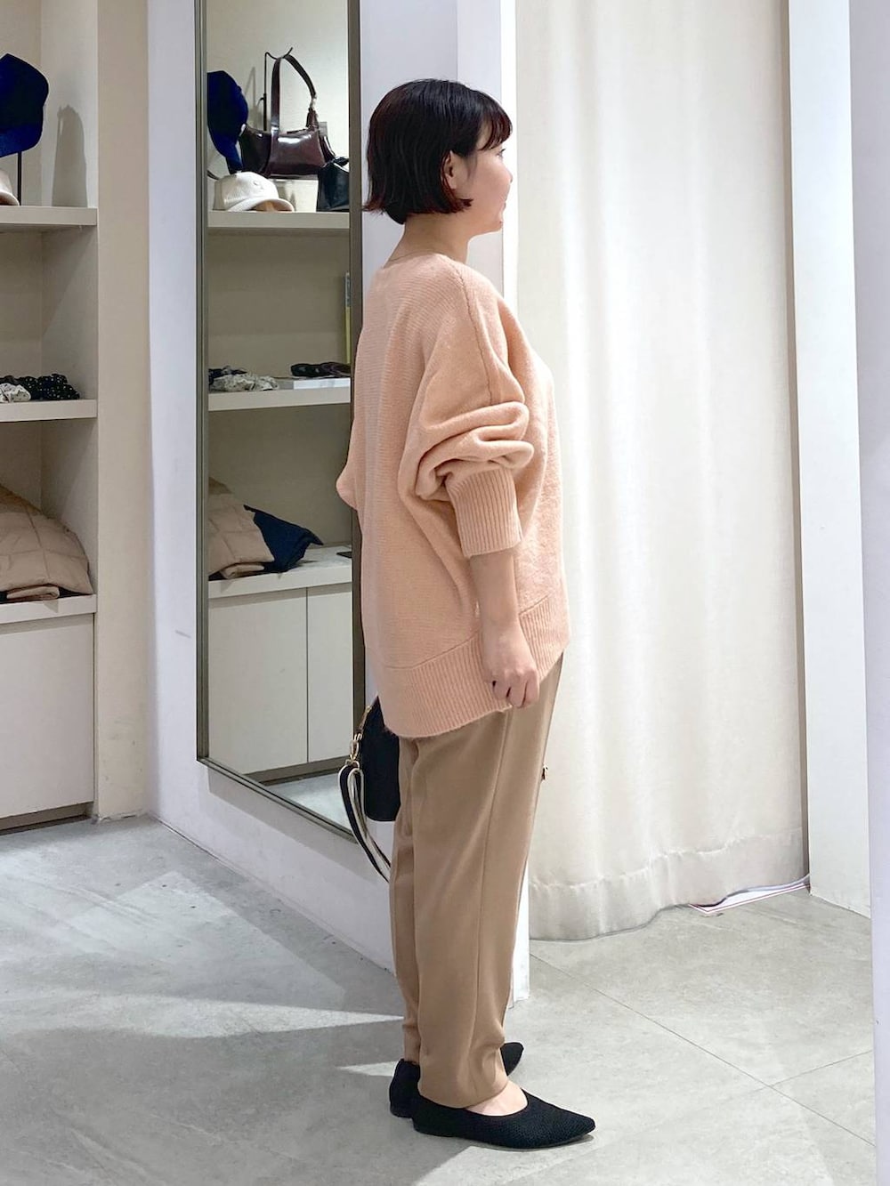 ブラック系のハンドバッグ、ピンク系のニット/セーター、ベージュ系のスラックスを着用したレディースの秋コーディネートの2枚目の写真