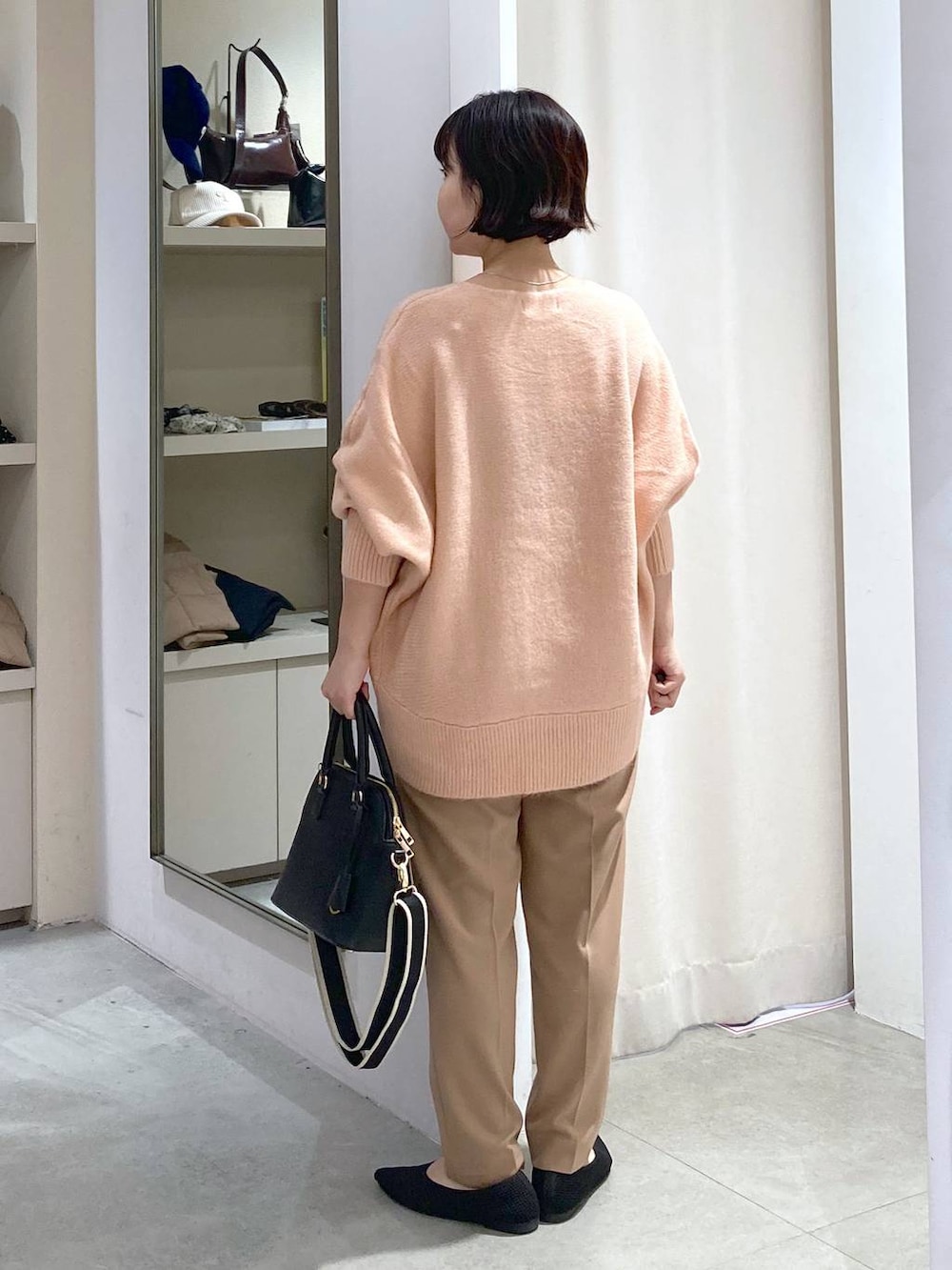 ブラック系のハンドバッグ、ピンク系のニット/セーター、ベージュ系のスラックスを着用したレディースの秋コーディネートの3枚目の写真