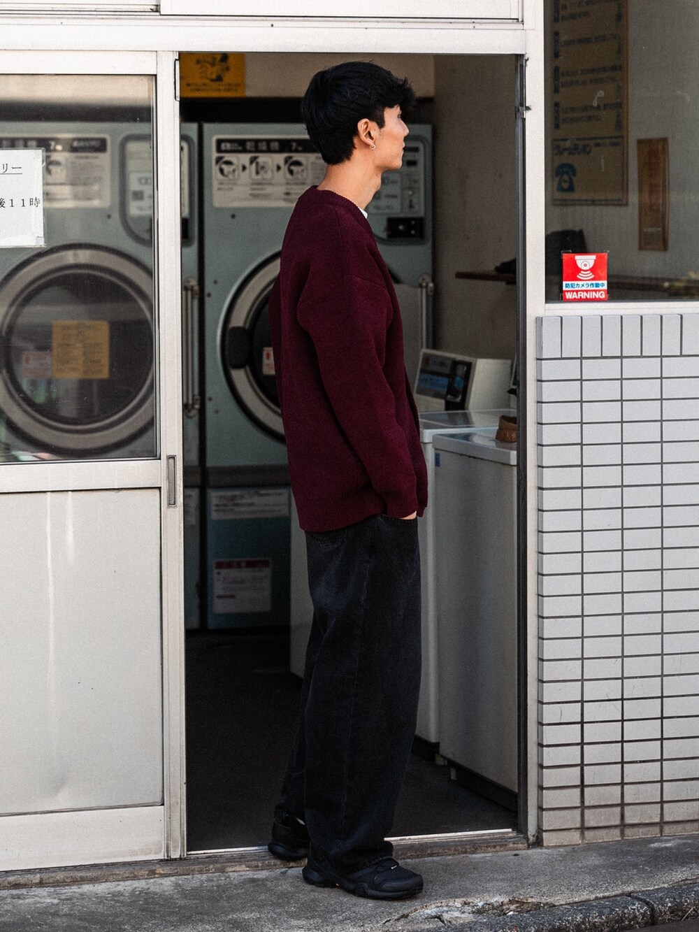 レッド系のカーディガン/ボレロ、ブラック系のデニムパンツ、ブラック系のスニーカーを着用したメンズの秋コーディネートの2枚目の写真