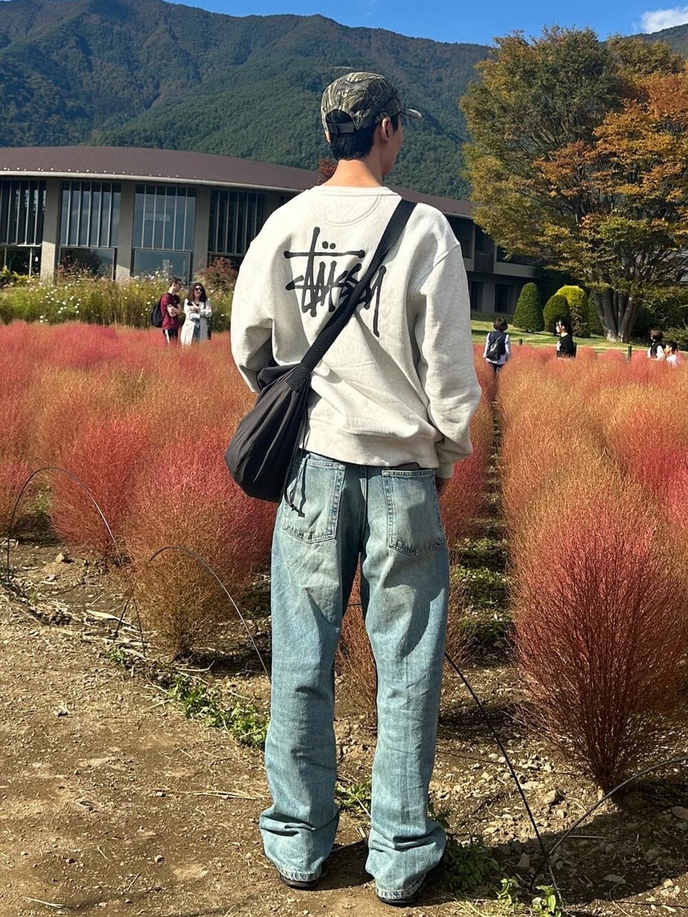 グレー系のスウェット、グレー系のショルダーバッグ、ブルー系のデニムパンツを着用したメンズの秋コーディネートの2枚目の写真