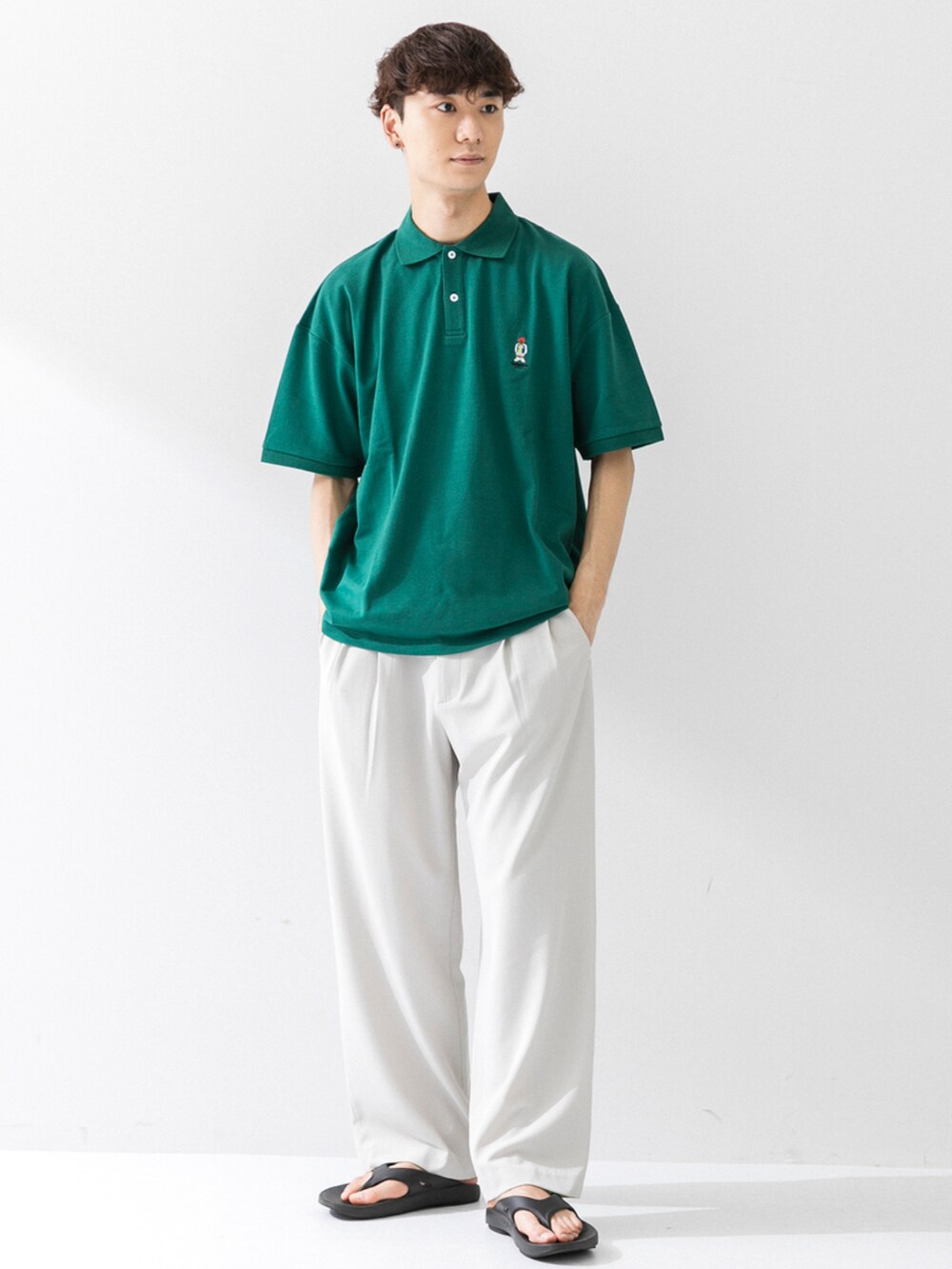 ブラック系のサンダル、ホワイト系のスラックス、グリーン系のポロシャツを着用したメンズの夏コーディネートの2枚目の写真