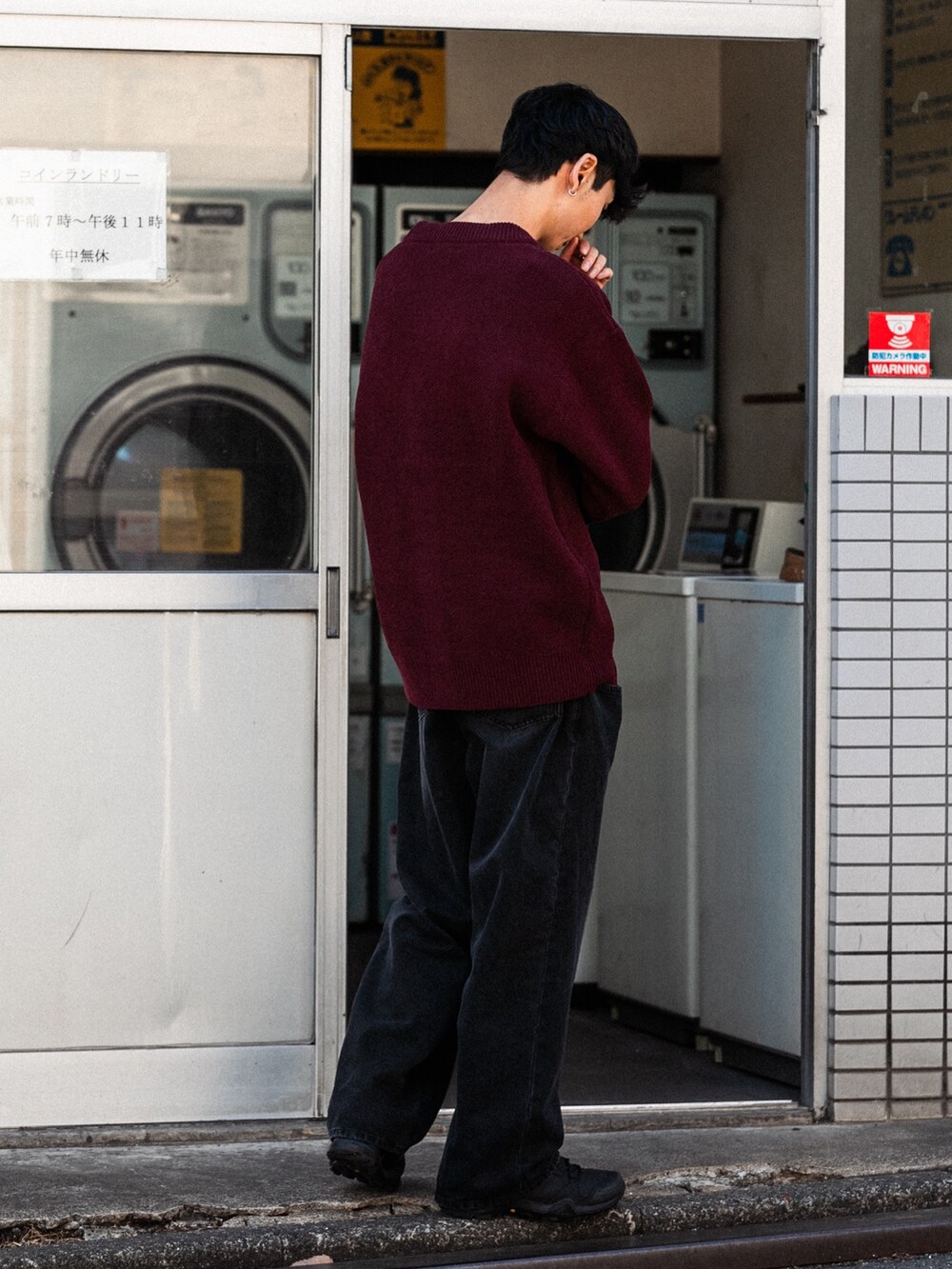 レッド系のカーディガン/ボレロ、ブラック系のデニムパンツ、ブラック系のスニーカーを着用したメンズの秋コーディネートの3枚目の写真