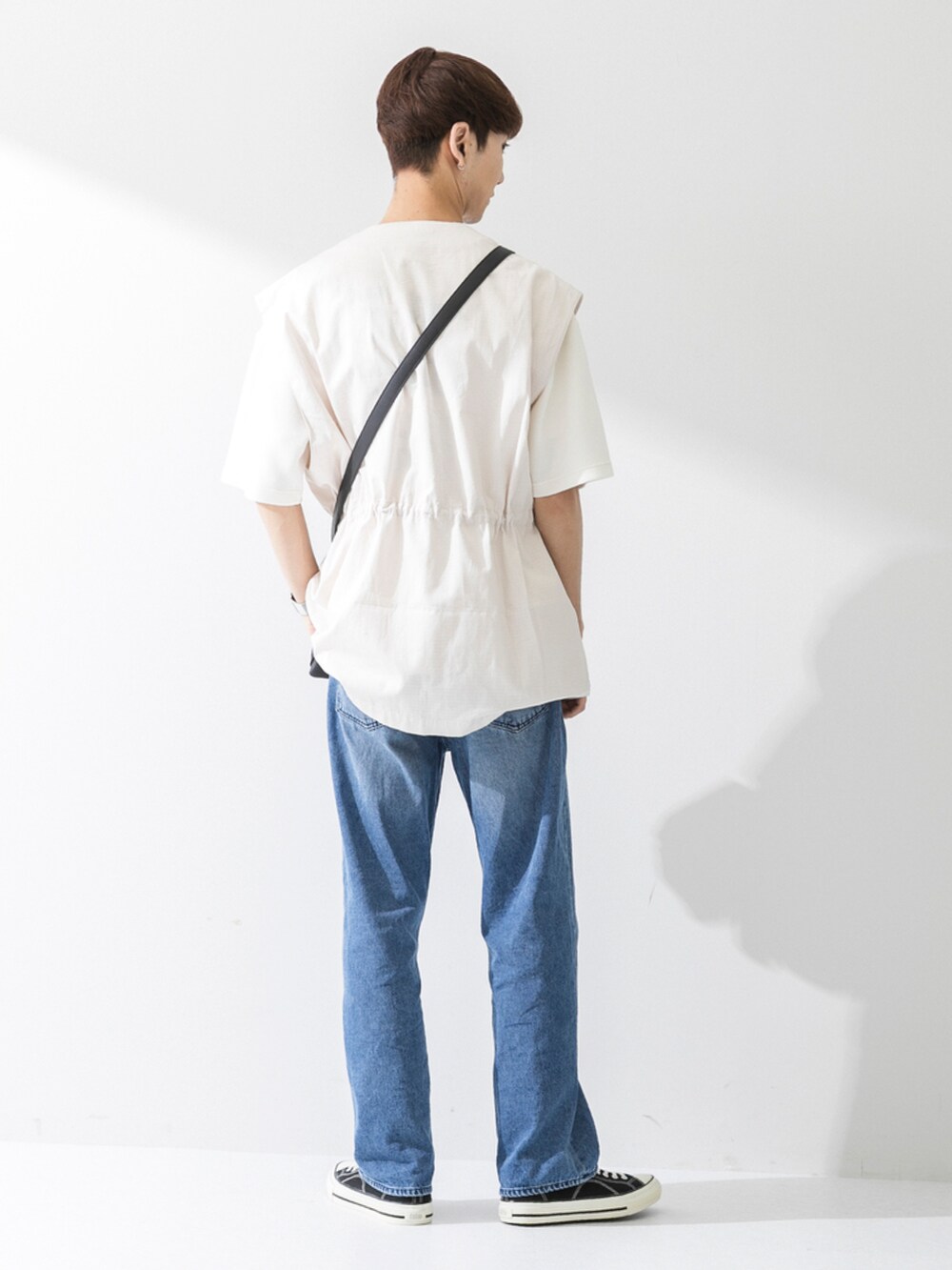 ブラック系のスニーカー、ブルー系のデニムパンツ、ブラック系のショルダーバッグを着用したメンズの夏コーディネートの2枚目の写真