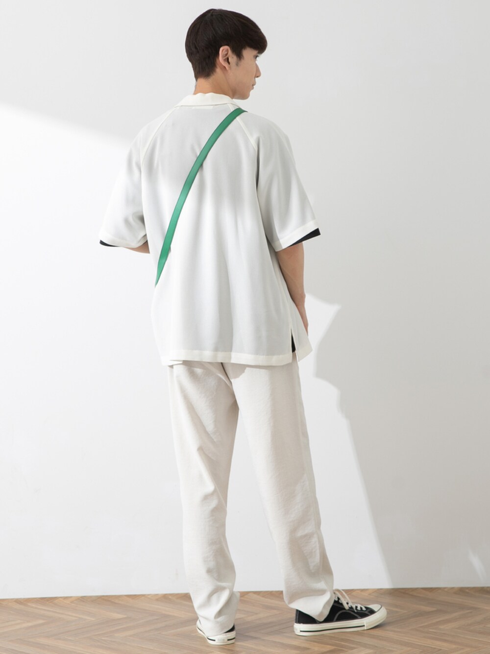 ブラック系のスニーカー、ホワイト系のスラックス、グリーン系のショルダーバッグを着用したメンズの春コーディネートの2枚目の写真