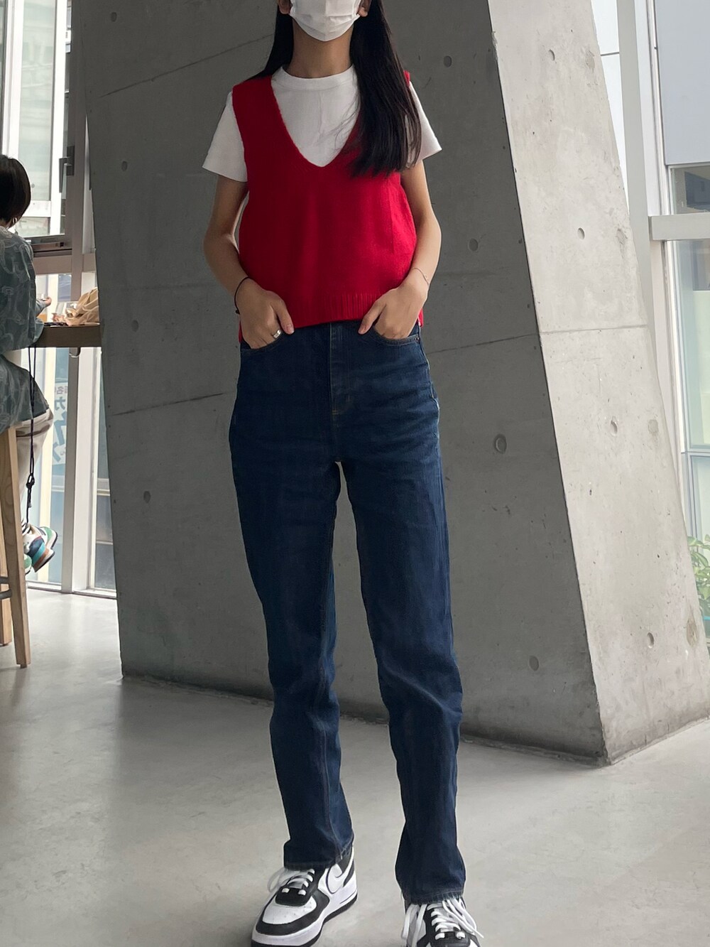 レッド系のベスト、ブルー系のデニムパンツ、ホワイト系のスニーカーを着用したレディースの秋コーディネートの2枚目の写真