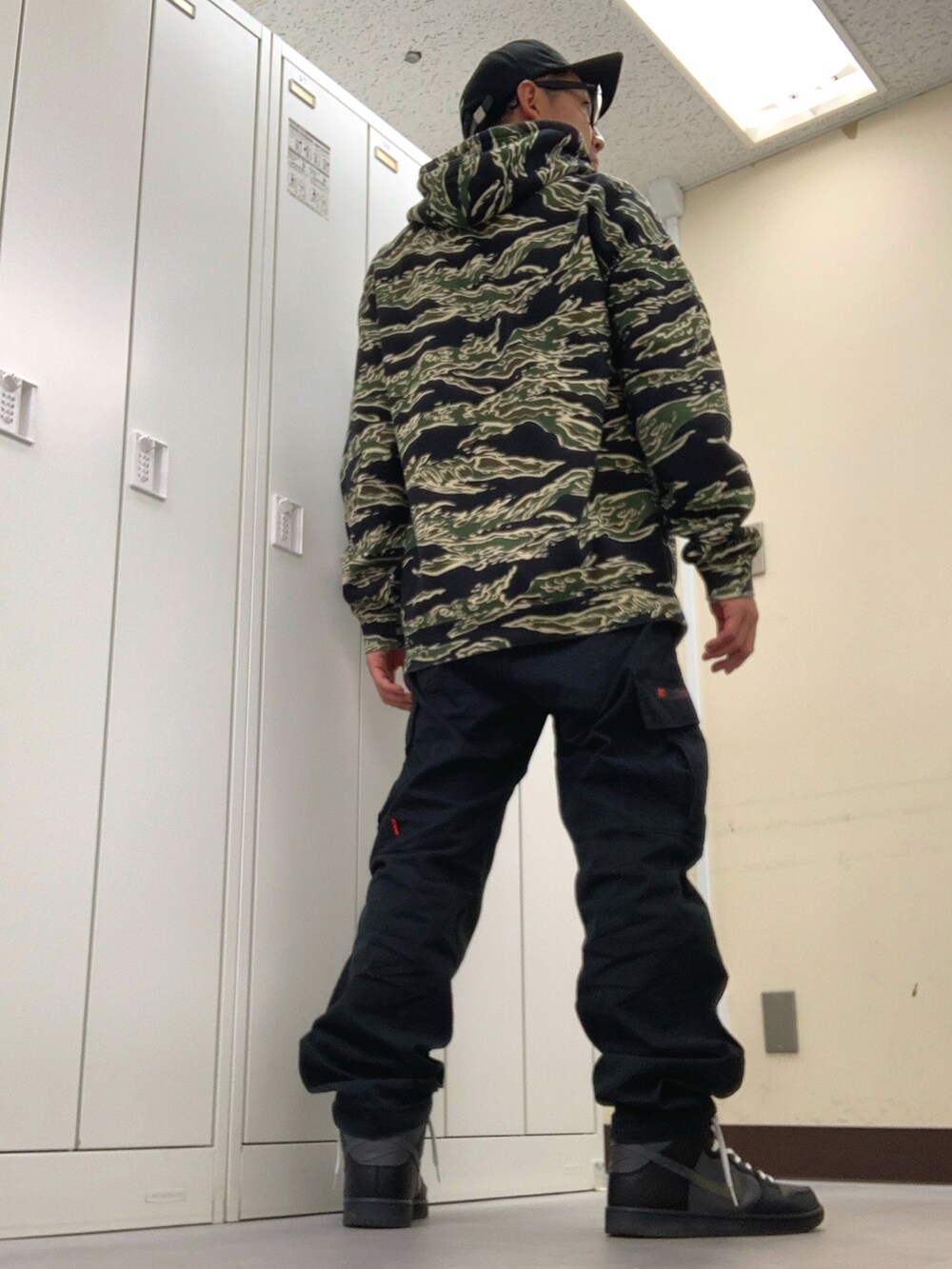 グリーン系のパーカー、ブラック系のカーゴパンツ、ブラック系のスニーカーを着用したメンズの秋コーディネートの3枚目の写真