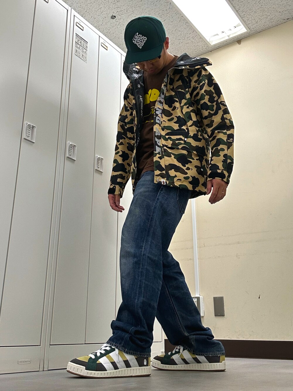 イエロー系のマウンテンパーカー、ブルー系のデニムパンツ、グリーン系のスニーカーを着用したメンズの秋コーディネートの2枚目の写真