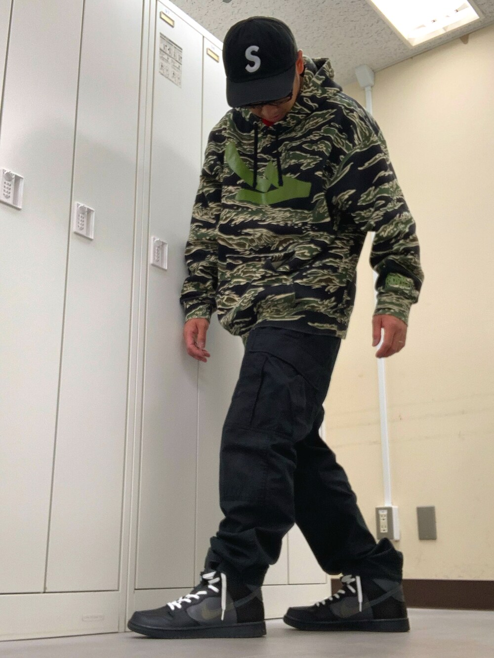 グリーン系のパーカー、ブラック系のカーゴパンツ、ブラック系のスニーカーを着用したメンズの秋コーディネートの2枚目の写真