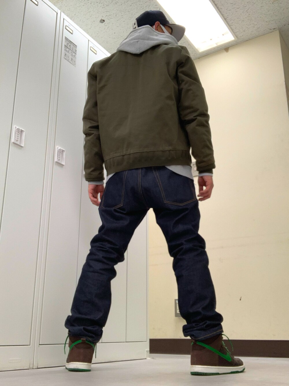 グリーン系のミリタリージャケット、ブルー系のデニムパンツ、ブラウン系のスニーカーを着用したメンズの秋コーディネートの2枚目の写真