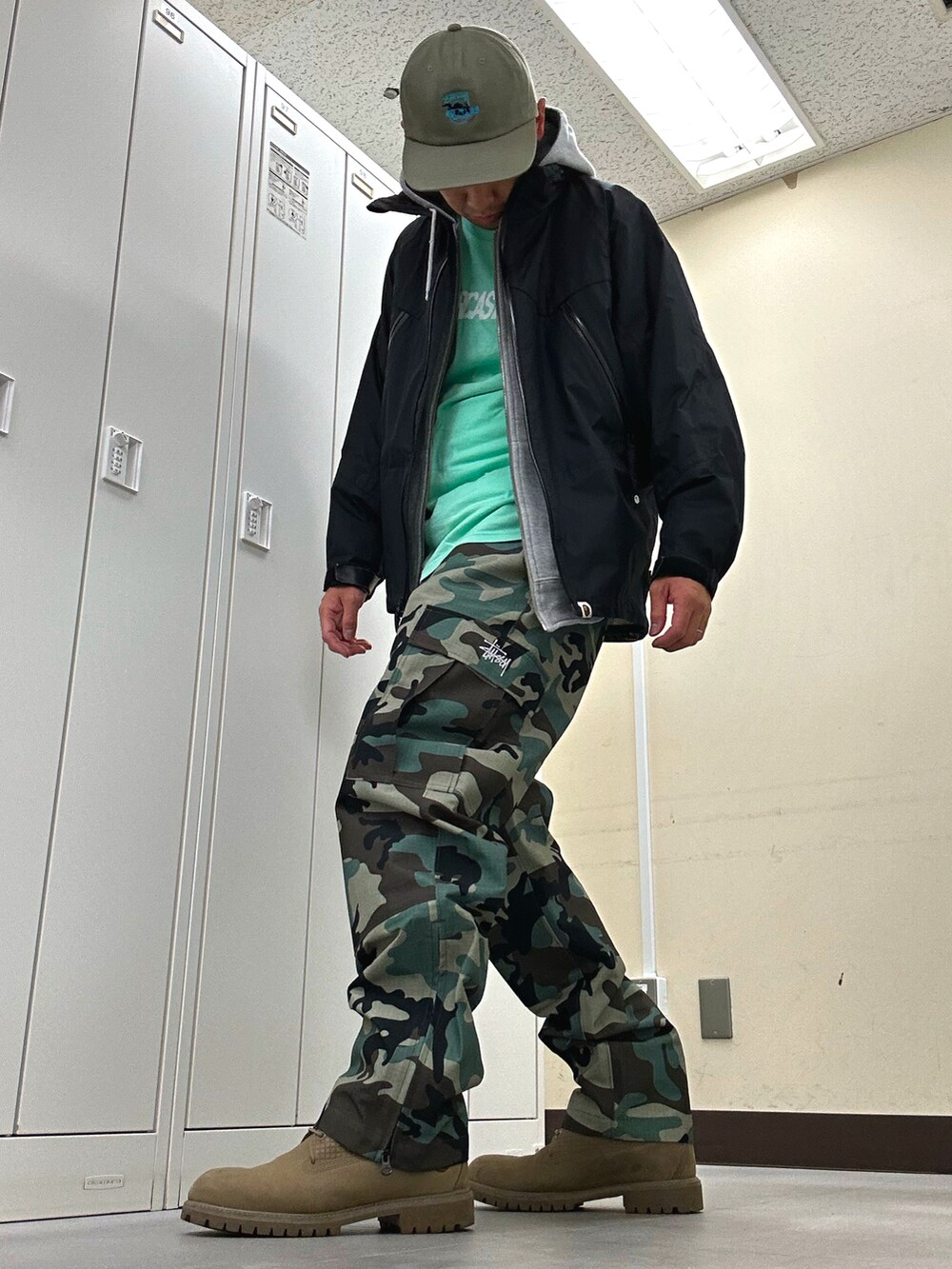 ブラック系のナイロンジャケット、グリーン系のTシャツ/カットソー、グリーン系のカーゴパンツを着用したメンズの春コーディネートの2枚目の写真