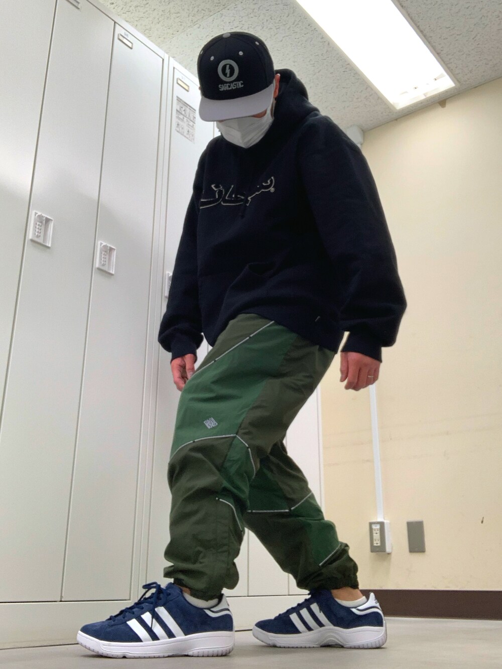 ブラック系のパーカー、グリーン系のその他パンツ、ブルー系のスニーカーを着用したメンズの春コーディネートの2枚目の写真