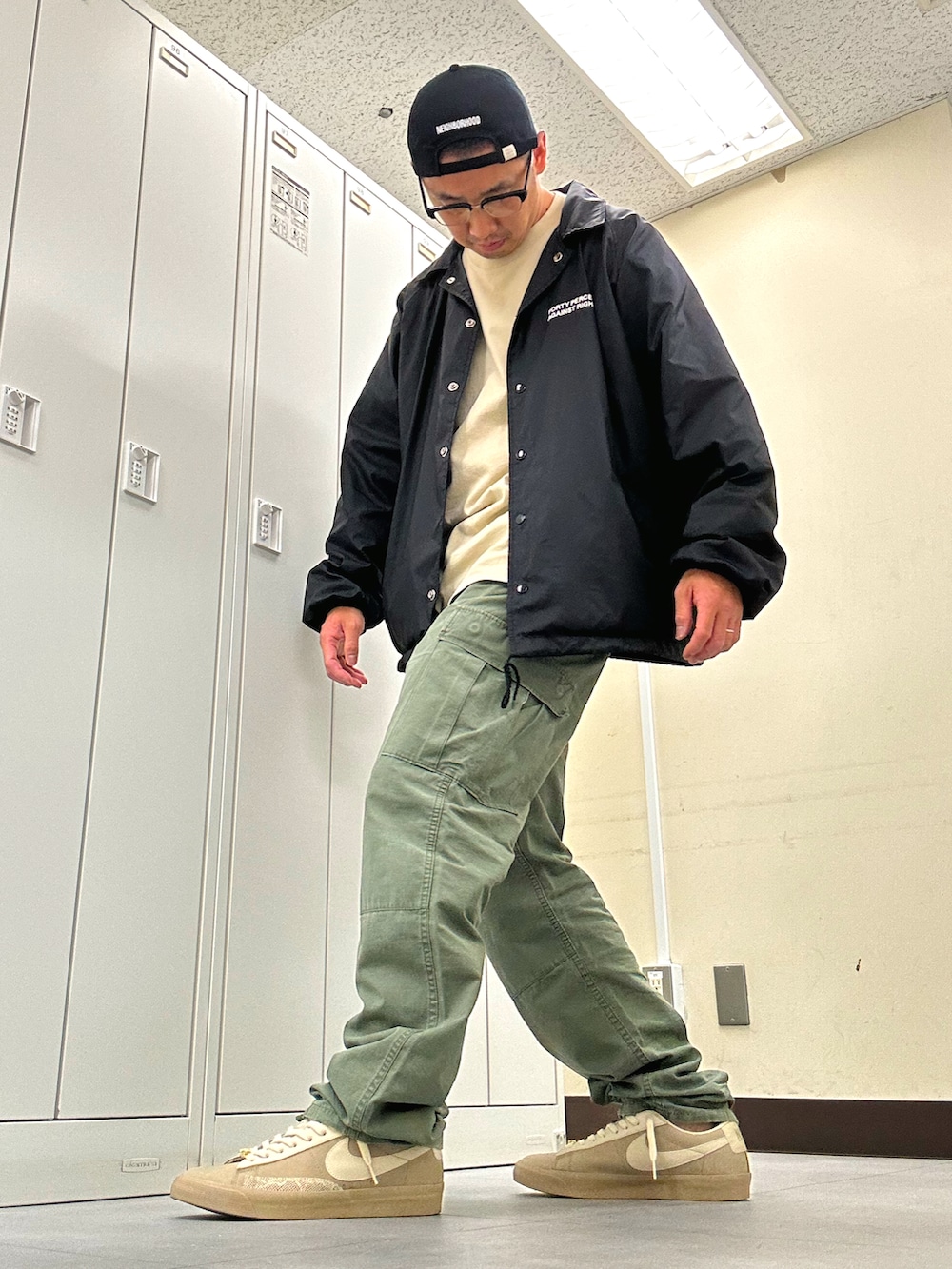 ブラック系のナイロンジャケット、ベージュ系のスニーカー、グリーン系のカーゴパンツを着用したメンズの夏コーディネートの2枚目の写真