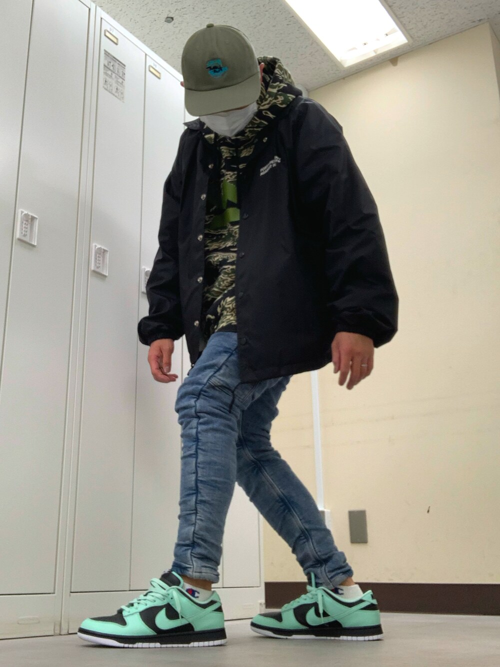 グリーン系のパーカー、ブラック系のナイロンジャケット、ブルー系のデニムパンツを着用したメンズの春コーディネートの2枚目の写真