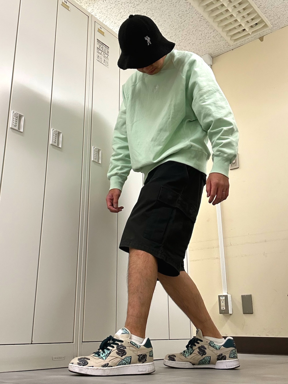 グリーン系のスウェット、ブラック系のカーゴパンツ、ベージュ系のスニーカーを着用したメンズの春コーディネートの2枚目の写真