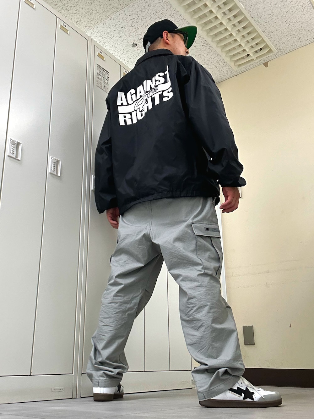ブラック系のナイロンジャケット、グレー系のカーゴパンツ、ホワイト系のスニーカーを着用したメンズの春コーディネートの3枚目の写真