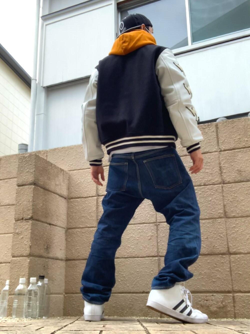 オレンジ系のパーカー、ブラック系のスタジャン、ブルー系のデニムパンツを着用したメンズの秋コーディネートの2枚目の写真