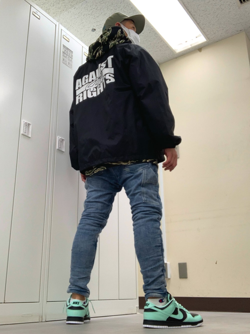 グリーン系のパーカー、ブラック系のナイロンジャケット、ブルー系のデニムパンツを着用したメンズの春コーディネートの3枚目の写真