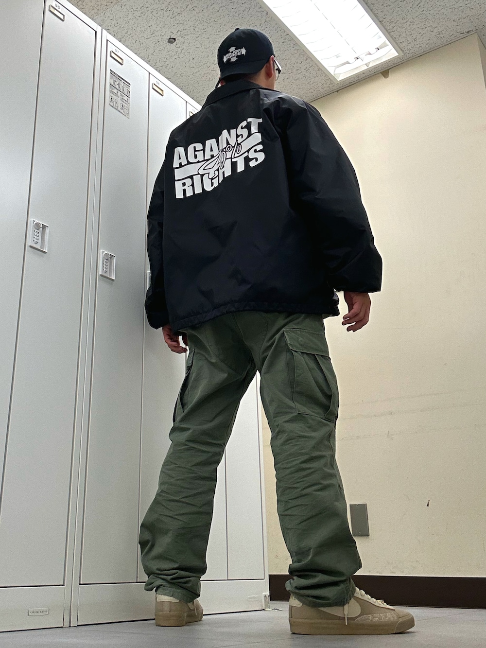 ブラック系のナイロンジャケット、ベージュ系のスニーカー、グリーン系のカーゴパンツを着用したメンズの夏コーディネートの3枚目の写真