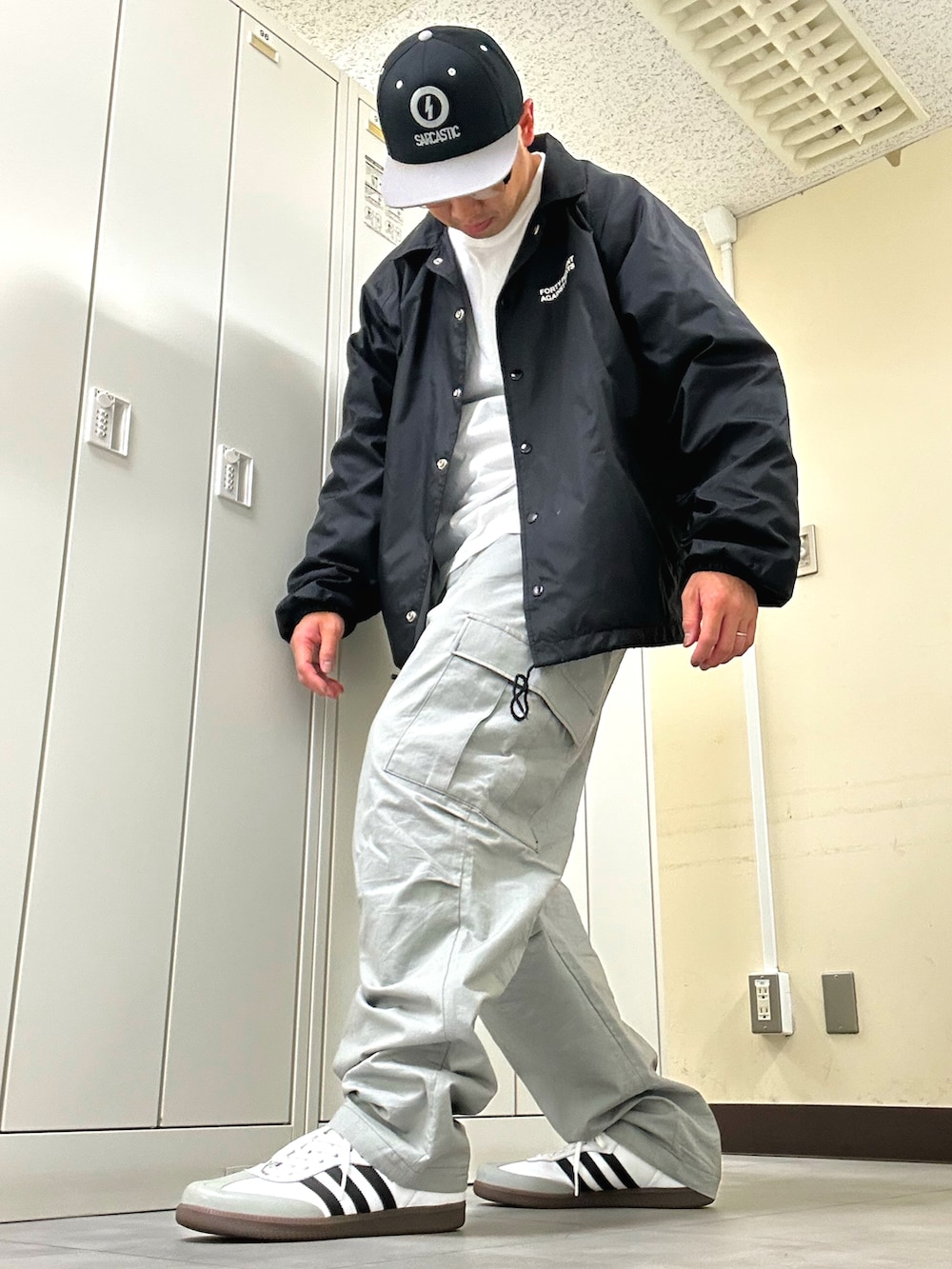 ブラック系のナイロンジャケット、グレー系のカーゴパンツ、ホワイト系のスニーカーを着用したメンズの春コーディネートの2枚目の写真