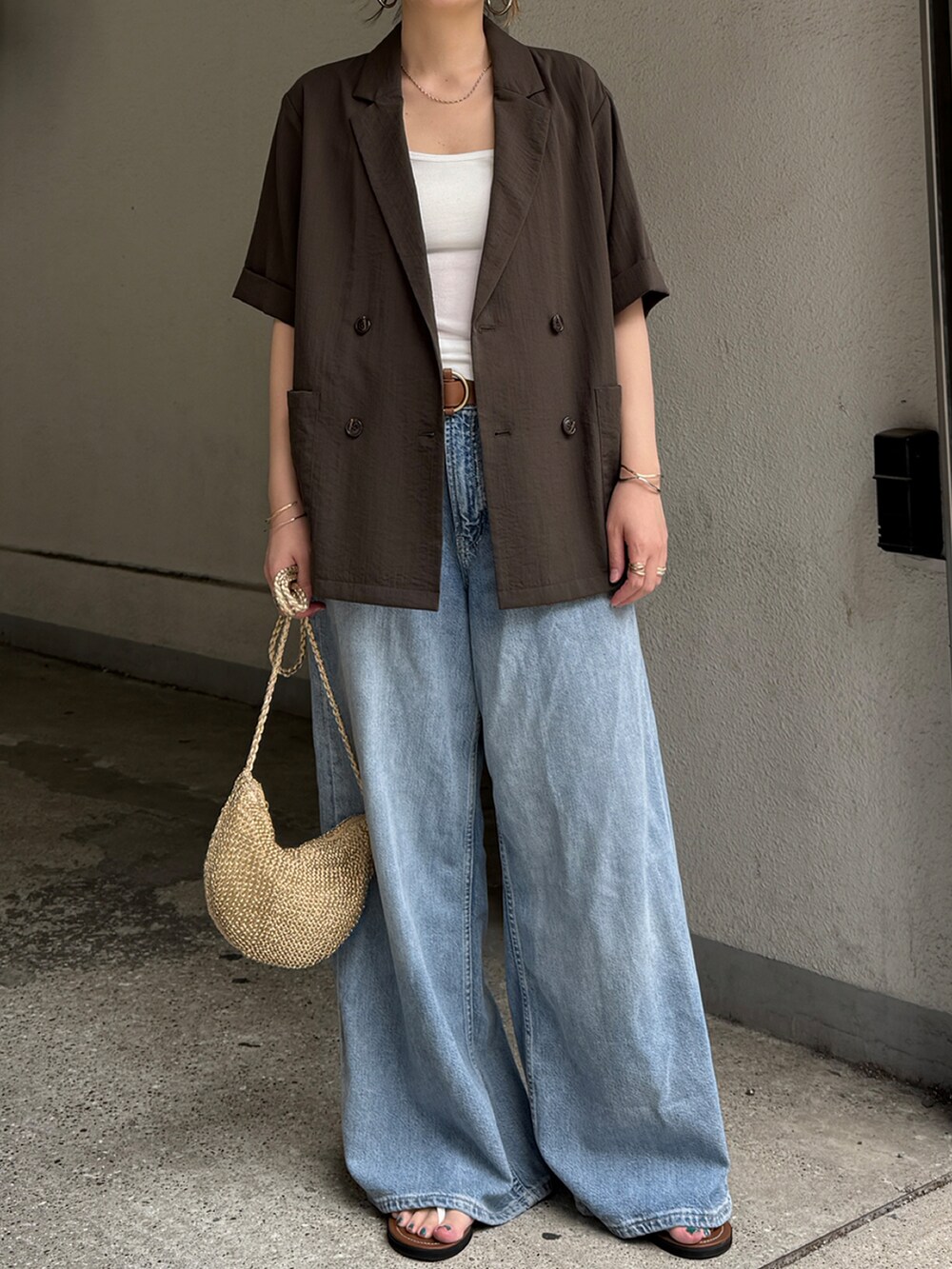 ブラウン系のテーラードジャケット、ブルー系のデニムパンツ、ゴールド系のショルダーバッグを着用したレディースの夏コーディネートの2枚目の写真