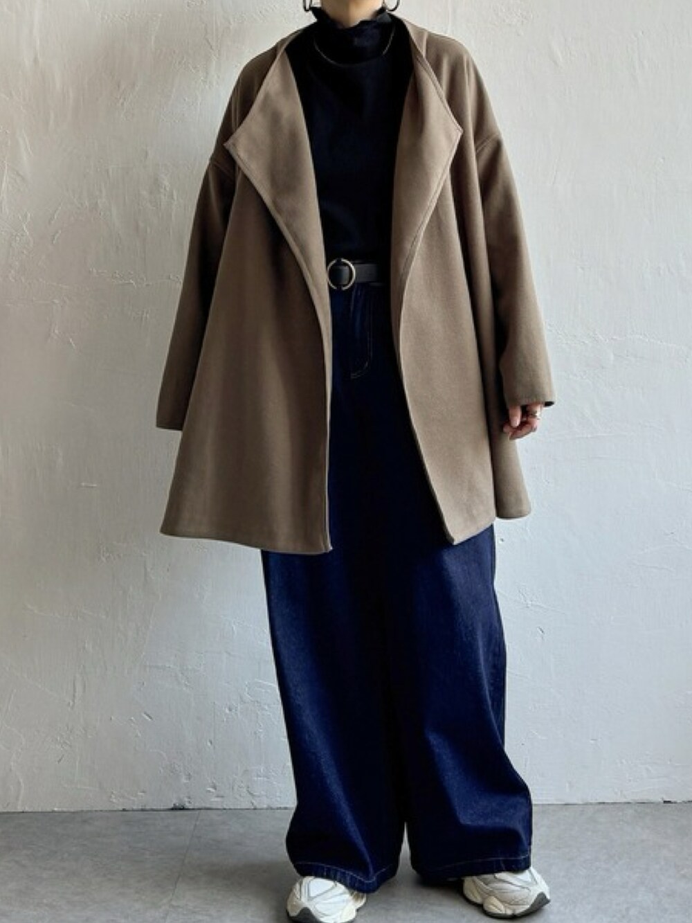 ブラウン系のノーカラーコート、ブルー系のデニムパンツ、ホワイト系のスニーカーを着用したレディースの冬コーディネートの2枚目の写真