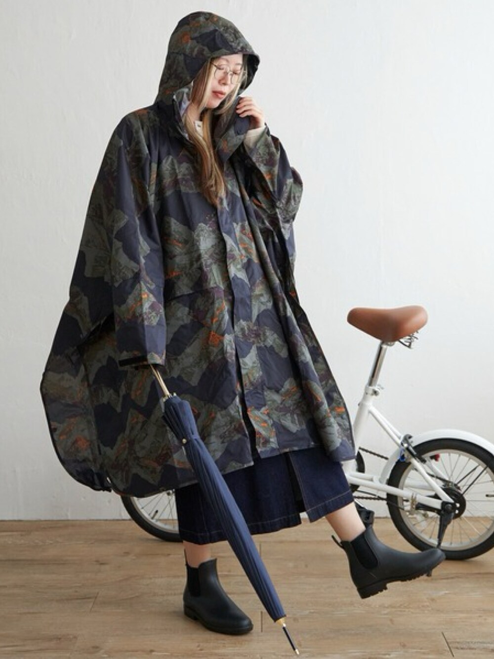 ブルー系のスカート、ブラック系のレインシューズ、グリーン系のレインコート/ポンチョを着用したレディースの春コーディネートの3枚目の写真