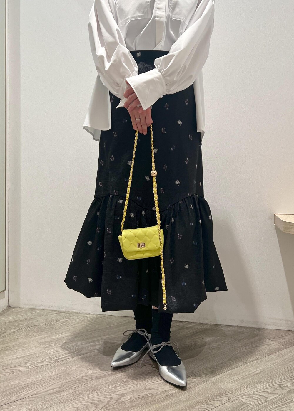 シルバー系のパンプス、イエロー系のショルダーバッグ、ブラック系のスカートを着用したレディースの冬コーディネートの5枚目の写真